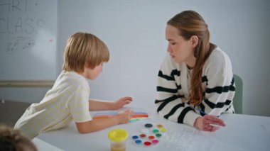 Sanat öğretmeni, öğrenciye atölyede palette yardım ediyor. Çağdaş kadın öğretmen oditoryumda küçük bir sanatçıyla resim çiziyor. Stüdyoda çocuklara resim öğreten yaratıcı bayan ressam. Yaratıcılık kavramı