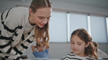 Işık sınıfı öğretmenini dinleyen kız. Yakın plan. Okul öğretmeninin öğrenciye okulda sınıf çalışması için yardım etmesi. Gülümseyen liseli kız deftere bakıp ders çalışıyor. Masada oturan kız öğrenci. 
