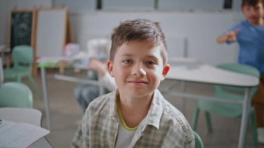 Neşeli okul çocuğu sınıf portresi dersinde kamera karşısında poz veriyor. Mutlu gülümseyen çocuk kabinede yakın plan eğitim veriyor. Küçük çocuk okulda oditoryumda öğreniyor. Sınıf arkadaşlarıyla neşeli bir öğrenci.