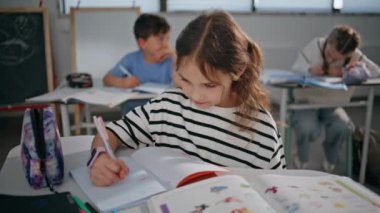 Sınıfta elinde kalem tutan küçük bir kız. Ciddi bir liseli kız cevap yazarak ders dinliyor. Akıllı çocuk okul salonunda masa başında oturup öğreniyor. Düşünceli özenli öğrenci eğitimi.