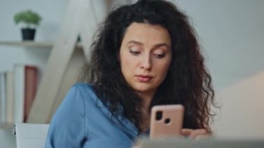 Modern ofiste cep telefonuna bakan sürpriz kadın. Rahatlamış bir kadın portresi, internetten akıllı telefonlara bakmaktan keyif alıyor. Kendine güvenen iş kadını patron iş yerinde online dinlenme sandalyesine mesaj atıyor..