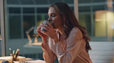Profesyonel kadın gece ofisinde mola veriyor. İşten sonra kahve içen, rahatlayan bir kadın. Gülümseyen sakin yönetici masasında sükunetin keyfini çıkartıyor. İşçi çayını yudumluyor