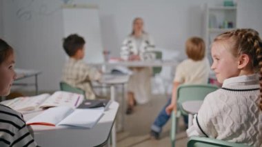 Akıllı çocuklar ilkokulun arka planında masalarında oturup öğreniyorlar. Beyaz tahtanın yanında konuşan bulanık kadın öğretmen sınıf odasında sorular soruyor. Oditoryumda okuyan bir grup zeki çocuk.