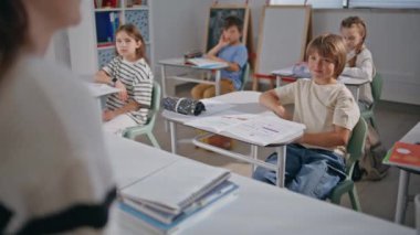 Bayan öğretmen sınıfta öğrencilerle konuşuyor. Yakın çekim. İlkokulda birlikte okuyan öğrenciler. Kabinedeki öğrencilere ders hakkında bilgi veren tanınmamış bir öğretmen 