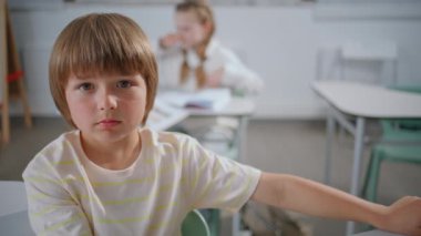 İlkokulda okuyan zeki bir öğrenci. Ciddi sarışın çocuk, kameraya bakıyor ve ders portresinin önünde oturuyor. Sınıfta zeki bir öğrenci dinleme öğretmeni. Sakin okul çocuğu sınıfta kendini meraklı hissediyor 