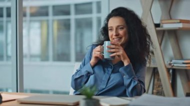 Gülümseyen iş kadını sandalyede kahve içiyor. Yakın plan gevşemiş yönetici ajans buro 'da huzur içinde dinleniyor. Güzel esmer. Gelecekteki başarı planlama projesini yönetiyor..