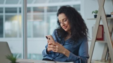 Gülümseyen yönetici iş yerinde cep telefonuna bakıyor. Rahat iş kadını modern ofiste cep telefonuna mesaj atıyor. Neşeli yönetici ağ kurulumu koltukta dinleniyor. Şirket çalışanı ara verdi.