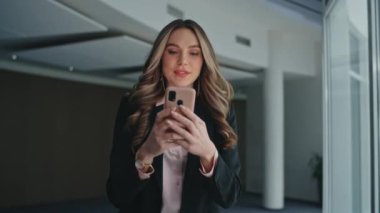 Çevrimiçi yürüyüş ofisinde mutlu yönetici mesajları. Kapalı çekim gülümseyen kadın akıllı telefonlara göz atıyor. Güzel, rahat iş kadını meslektaşına el sallıyor. İşteki kendine güvenen patron..