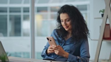 Masada akıllı telefon kullanan rahat bir çalışan. Gülümseyen iş kadını mesajlaşması sosyal uygulamalarda online iletişimin tadını çıkarıyor. Ofis koltuğunda dinlenen başarılı bir profesyonel cep telefonu..