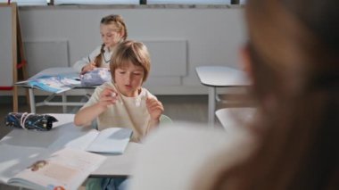 Zeki bir öğrenci, masa başında öğrenme dersine cevap veriyor. Düşünceli, şirin bir ilkokul öğrencisi, elinde kalem tutarak egzersiz kitabına yazmış. Anaokulu öğrencisi. Sınıfta, masada oturuyor. 