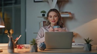 Akşam çalışanı masada kahve fincanı tutuyor. Müdür işten sonra ara veriyor. Geceleri gülümseyen güzel yönetici koltukta dinleniyor dizüstü bilgisayara bakıyor. Başarılı olduğunu düşünen mutlu iş kadını.