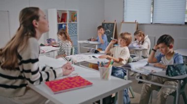 Zeki okul çocukları derslerde yakın çekimde eğitimci ararlar. Gülümseyen öğretmen ilkokul sınıfındaki çocuklara sorular soruyor. Okul öğretmeninin sınavına olumlu cevap veren mutlu öğrenciler. 