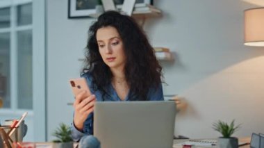 Gece işyerinde SMS okuyan mutlu bir iş kadını. Yönetici cep telefonunu kontrol ediyor. Neşeli kıvırcık yönetici modern ofiste mesaj alıyor. Bilgisayarda çalışan gülümseyen kadın.