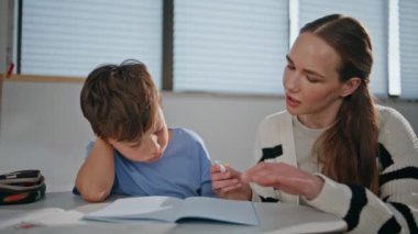 Sınıftaki çocuğa yardım eden özenli bir öğretmen. Yakın plan. İlkokulda ders alan küçük bir öğrenci. Bayan eğitimci okul çocuğuyla kitap çözme sınavı yazıyor. Eğitim kavramı