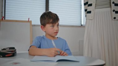 Akıllı çocuk yakın çekimde kitapçığı yazıyor. Masada ders çalışmayı öğrenen küçük bir öğrenci. Anaokulu öğrencisi sınıfta ders çalışıyor. Okulda notlar alıyor. Genç öğretmen erkek öğrenciye yardım ediyor.