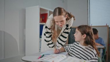 Bayan öğretmen sınıfta kıza yakın çekimde yardım ediyor. Okul öğrencisiyle konuşan genç bir bayan, sonuçları kontrol etmek için ders çalışıyor. Gülümseyen öğretmen kabinede öğrenciyle konuşuyor. Eğitim kavramı