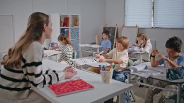 Öğretmen hanım sorular soruyor. Dersi kapatıyoruz. Grup öğrencileri okulda öğreniyor. Aktif sınıf arkadaşları sıralarında gülümsüyor. Dost canlısı genç bayan öğretmen sınıfta çocuklarla konuşuyor.