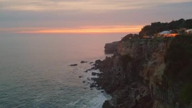 Köpüklü okyanus suyunun üzerindeki güzel sakin sahil günbatımı kayalık kıyılarda yavaş çekimde sıçrıyor. Karanlık dalgalı deniz yüzeyinde gün batımından sonra altın gökyüzü. Hava fırtınalı dalgalar yüksek kayalıklara çarpıyor.