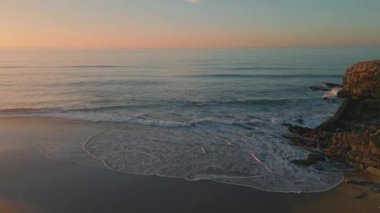 Pastel gün doğumu okyanus manzarası. Sabah sahilinde taşlaşmış deniz kıyılarını köpüklü dalgalar yıkıyor. Fırtınalı deniz dalgaları doğanın arka planında kayalık kıyıları kırıyor. Seyahat tatili deniz manzarası kavramı 