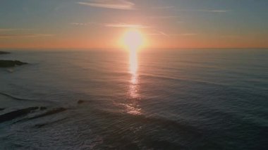 Sabah deniz dalgaları yavaş çekimde sıçrıyor. Güneşin doğuşunda dalgalanan deniz dalgaları. Turuncu güneş ışınlarının altında yüzen manzaralı derin su. Karanlık okyanus yüzeyi pastel ışığı yansıtıyor. 