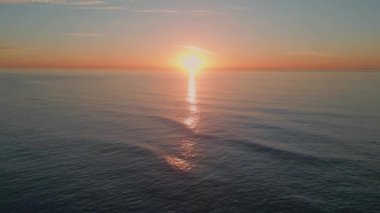 Akşamları deniz dalgaları yavaş çekimde sıçrıyor. Gün batımında dalgalanan deniz dalgaları. Turuncu güneş ışınlarının altında yüzen manzaralı derin su. Karanlık okyanus yüzeyi pastel ışığı yansıtıyor. 
