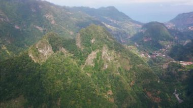Görkemli dağlar yemyeşil vadilerin üzerinde yükseliyor manzaralı hava manzarası. Yamaçta yuva yapmış kırsal köy sakin kırsal bölgeleri gösteriyor. Engebeli arazide yeşillik manzaralı manzaralar sunar..