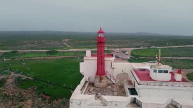 Kasvetli manzara okyanus feneri drone görüntüsü. Güzel sahil fenerinin üzerinde bulutlu bir sabah gökyüzü. Kırmızı navigasyon kulesi olan beyaz bina harika bir sahil kenarında otoban ile duruyor. Deniz güzelliği 