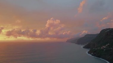 Okyanus dalgaları hava manzarası ile yıkanan kıyı uçurumlarının üzerinde güneşli bir gün doğumu. Renkli gün doğumu bulutları olan manzaralı bir yer. Sakin deniz yüzeyinin üzerinde altın renkli bir güneş ışığı. Rocky kıyı şeridi