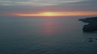 Okyanus ufkunun üzerinde turuncu günbatımı gökyüzü. Sakin deniz dalgalarının çok yavaş çekimde dalgalanan deniz dalgalarına yansıyan resimli yaz günbatımı. Altın güneş sakin bir deniz akşamında batıyor