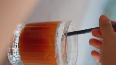 Caddedeki kafede saman gibi soğuk bir kokteylden içen tanınmamış bir kadın. Ahşap masada dikey olarak buz küpleriyle el çırpan kız içeceği. Genç restoran ziyaretçisi alkolün tadını çıkarıyor.