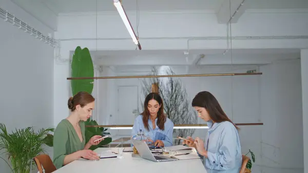 stock image Women team working project together in office. Creative managers drinking water checking smartphones at workplace. Girl specialist recording online arrangement message. Cooperation partnership concept