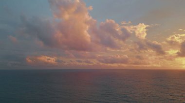 Bulutlu gökyüzü, sakin okyanus suyunun üzerinde, bulutlu günbatımında, hava manzarası. Huzurlu akşam deniz manzarası huzurlu bir atmosfer yaratıyor. Turuncu ufuk çizgisinin altında dalgalanan resim gibi deniz yüzeyi. Manzaralı deniz gün doğumu.