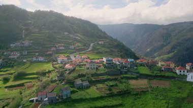 Portekiz köyü yemyeşil dağ yamaçlarına kurulmuş yemyeşil tarlalar ve kıvrımlı yollar hava manzaralı. Kırmızı kiremitli evler manzaralı kırsal alan yaratır. Kırsal yaşam için seyahat hedefi.