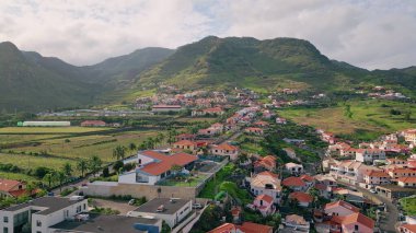 Akdeniz kırsalındaki insansız hava aracı resimli köy çatıları. Yeşil dağlarda kırmızı çatıları olan kıyı kasabası. Deniz kenarındaki binaların sakin ve güzel manzarası. Bulutların altındaki rahatlatıcı manzara