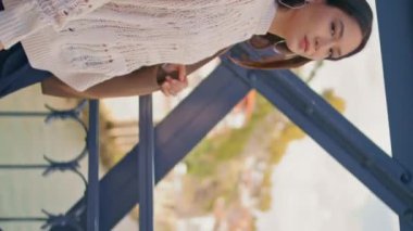 Yaz yürüyüşünde köprüden geçerken gülümseyen kendine güvenen bir kadın dikey video. Gevşemiş Asyalı kız bir omuz üzerinde gezen demir gölet inşaatında çanta tutuyor. Esmer genç bayan işe geri dönüyor.