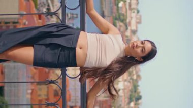 Seksi esmer kadın, yaz günü dikey doğrultuda poz veriyor. Baştan çıkarıcı kadın kamerayı nehir manzarasına çeviriyor. Uzun saçlı rahat bayan rüzgarlı havanın tadını çıkarıyor.