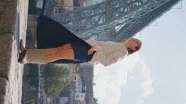 Romantik kadın güneşli gezinti güvertesinde tek başına yürüyor. Hayalperest kız kollarını kaldırıp yaz dikey çekimlerinin keyfini çıkarıyor. Kaygısız, mutlu bir kadın güzel şehir manzaralı nehir kenarına basıyor. Seyahat ve turizm kavramı