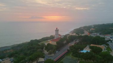 Kıyı fenerinde kasvetli bir hava var. Yeşil deniz kıyısı havası manzaralı. Sakin deniz ufkunun üzerinde portakal rengi bir gökyüzü. Güzel sahil kasabasına yerleştirilmiş modern deniz fenerinde muhteşem bir günbatımı parlıyor..