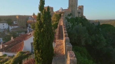 Eski kasaba havası boyunca uzanan taştan antik bir duvar. Kırmızı binaları yemyeşil yeşillikten ayıran ortaçağ şatosu. Alacakaranlık ışığı, tarihi kentin manzarasını güzelleştiriyor..