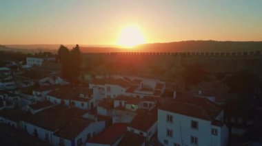 Gündoğumu parlayan ortaçağ şatosu Obidos eski Portekiz insansız hava aracı manzarası üzerinde yükseliyor. Tarihi duvarlarda ve köyün çatılarında altın şafak ışıkları. Antik mimari ve kırsal arazi üzerinde güneş.
