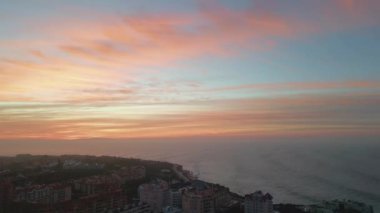 Güneşin doğuşu güzel kıyı şeridi hava manzarasına yerleştirilmiş kasabayı aydınlattı. Muhteşem turuncu gökyüzü güzel okyanusun üzerinde. Deniz suyu, sahil kentini çok yavaş çekimde yıkıyor. Alacakaranlıkta turuncu ufuk rahat tatil beldesinin üzerinde.