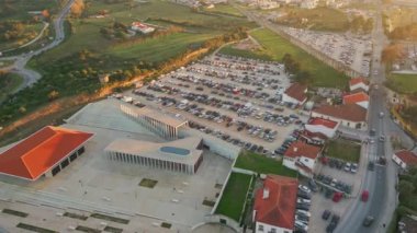 Arabaları ve araçları olan modern hava manzaralı park yeri. Mimari yapı kırsal alanda ayakta duruyor. Çevredeki binaların güzel kırmızı çatıları kırsal çevreye karışıyor.. 