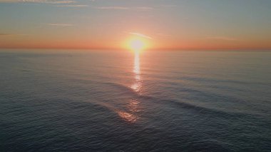 Akşamları deniz dalgaları yavaş çekimde sıçrıyor. Gün batımında dalgalanan deniz dalgaları. Turuncu güneş ışınlarının altında yüzen manzaralı derin su. Karanlık okyanus yüzeyi pastel ışığı yansıtıyor. 