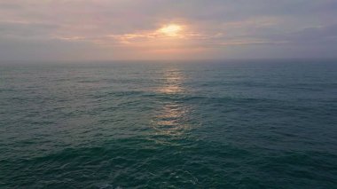 Okyanus suyunun üzerinde bulutlu bir akşam gökyüzü ağır çekimde dalgalanır. Drone yaz günbatımında güçlü sonsuz karanlık deniz manzarası. Deniz ufkunda asılı gri bulutlar güneş ışığını gizliyor. Huzur kavramı 