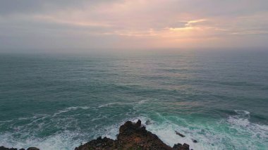 Bulutlu gökyüzü manzarasında altın gün batımı ışığıyla dramatik bir akşam deniz ufku. Güçlü, güzel okyanus dalgaları kasvetli siluet altında ağır çekimde yuvarlanıyor. Alacakaranlıkta derin karanlık deniz manzarası 