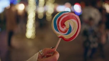 Renkli lolipop, gece vakti eğlence parkında kadınların elinde. Kimliği belirsiz bir kız Noel pazarında elinde şeker tutuyor. Parlak tatil ışıkları neşeli, rahat bir ortam yaratıyor..