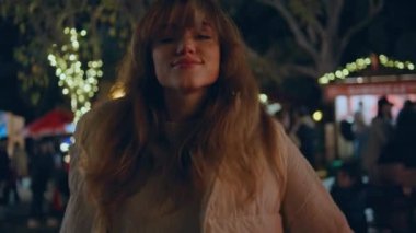 Noel pazarında eğlenen bir kadın. Kapanış gecesi. Kış festivali ışıklarında dans eden mutlu kadın kendini mutlu hissediyor. Neşeli kız tatilini dışarıda neşeli bir ruh haliyle kutluyor..