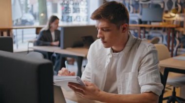 Ofisteki adam açık alanda defter yazarken not alıyor. Ciddi bir adam uzak bir iş yerindeki ajandaya işaret koyuyor. Modern iç mekanda kalem görünümlü bir not defteri tutan serbest çalışan. Çalışma konsepti 