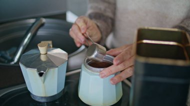 Kadın elleri Moka pot 'a kahve koyuyor. Yakın çekim için sabah içeceği hazırlıyor. Ev mutfağında tanınmayan bir kadın aromatik espresso yapıyor. Bilinmeyen ev hanımı, kuzinede kahve makinesi kullanıyor..