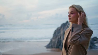 Sarışın model, takım elbise içinde okyanus batımı pozu veriyor. Magazin fotoğrafçısı, akşam kayalıklarında muhteşem bir kızın fotoğrafını çekiyor. Moda fotoğrafçılığında kumsalda çalışan seksi bayan.. 